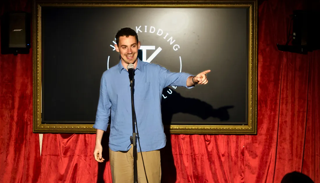 Comedian performing live stand-up in front of the Just Kidding Comedy Club backdrop at JK Comedy Club Leicester Square